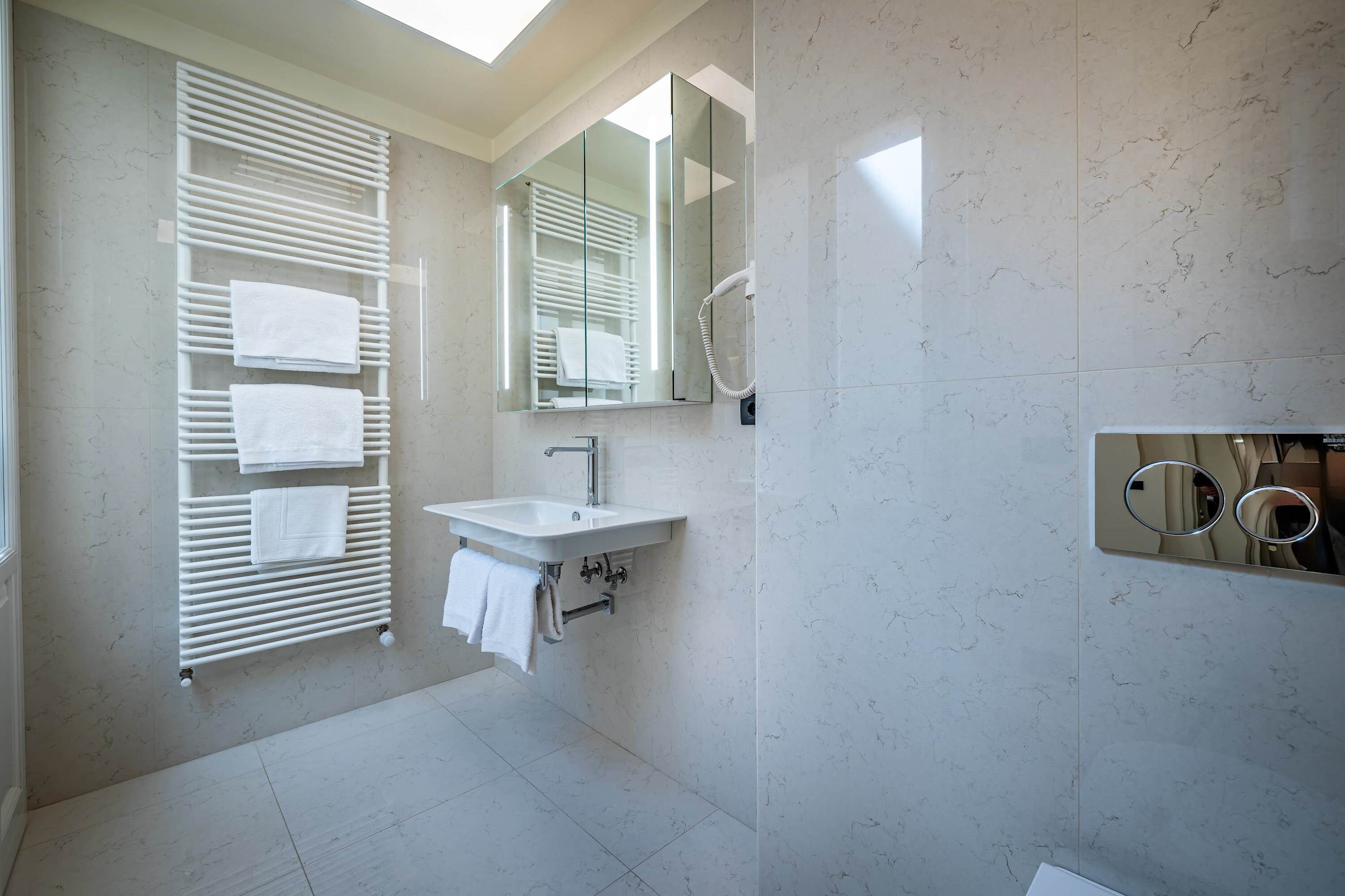 Une salle de bain moderne dotée d’un porte-serviettes intégré, d’un lavabo, d’un miroir et d’un espace douche.