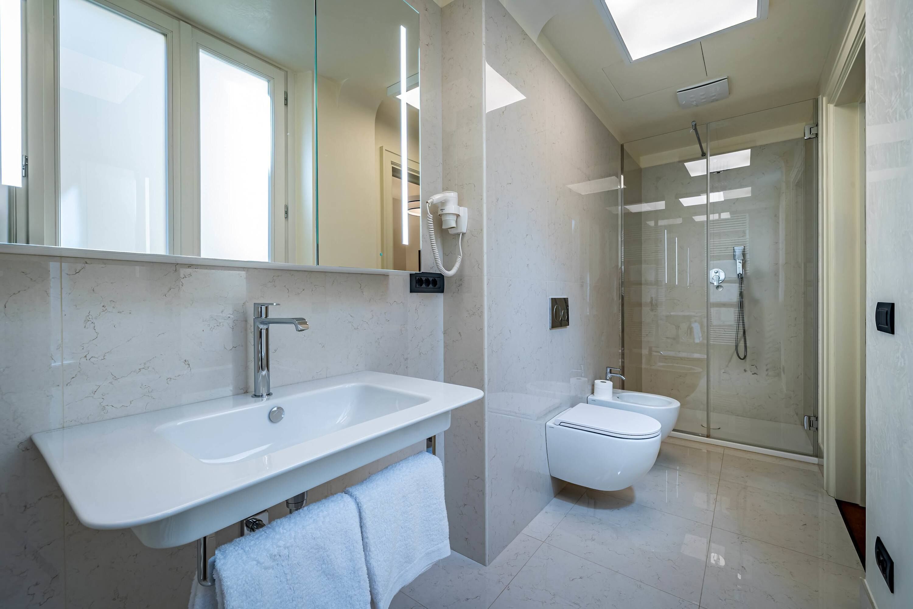 Un baño moderno con un espejo grande, un lavamanos, un inodoro y una ducha con mampara de cristal.