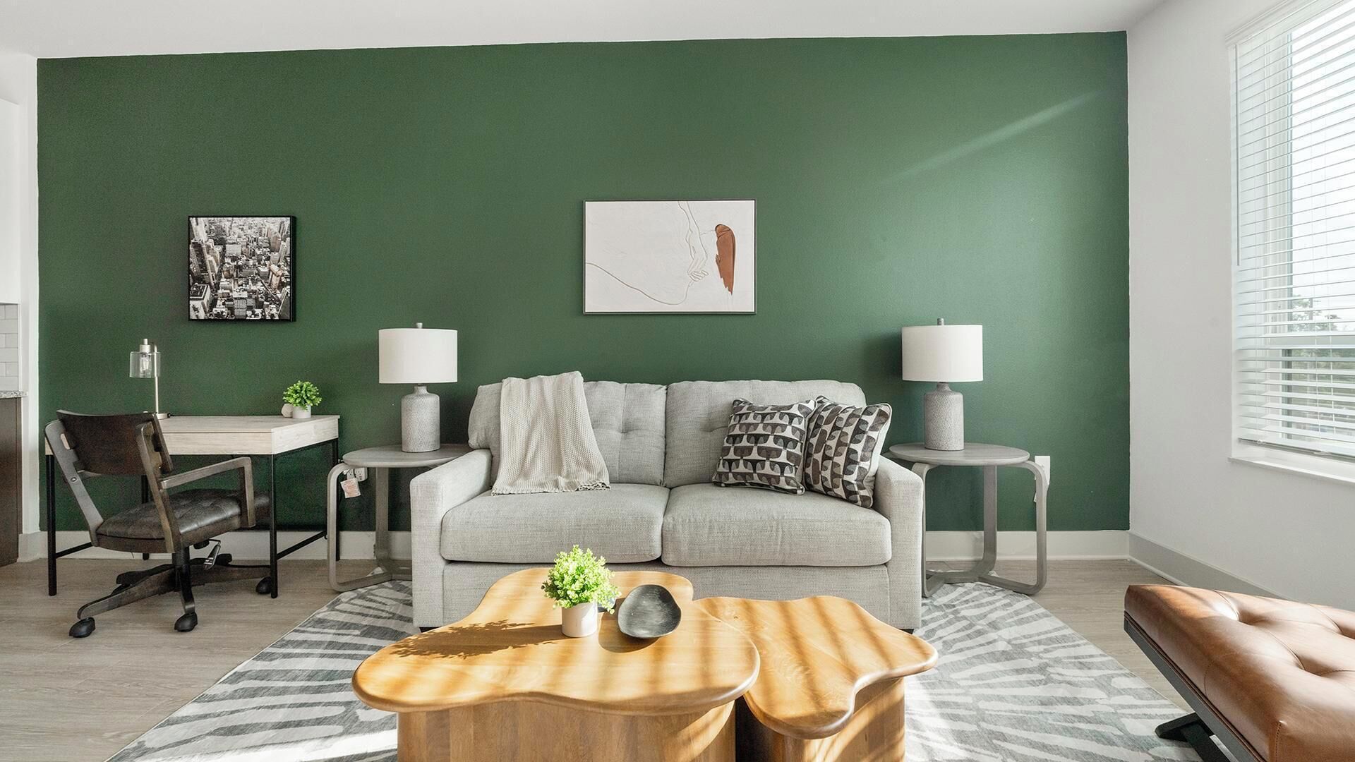 Ein modernes Wohnzimmer mit einer grünen Akzentwand, einem grauen Sofa, zwei Beistelltischen mit Lampen, einem Holztisch als Couchtisch, einem gemusterten Teppich und einer Bank.