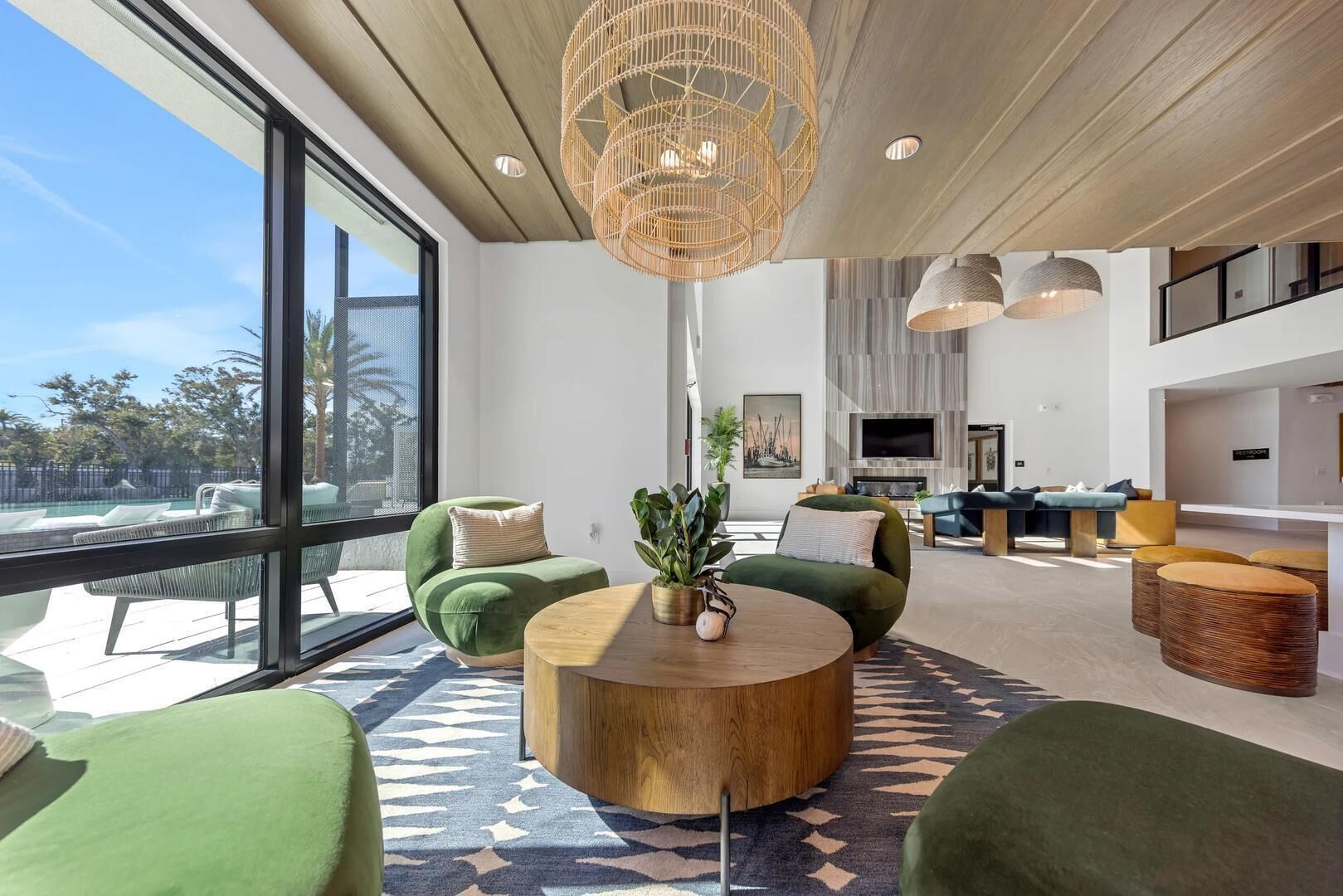 A spacious living area with a large window, a round wooden coffee table, and green upholstered seating.