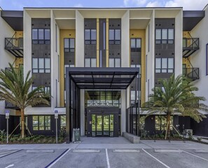 Un edificio moderno con un ingresso centrale, numerosi balconi e un'area di parcheggio.