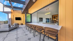 Ein moderner Außenbereich mit einer langen Bar, Korbstühlen und einer Couch.