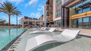 Ein moderner Poolbereich mit Liegestühlen, einer Palme und einem Gebäude mit großen Fenstern.