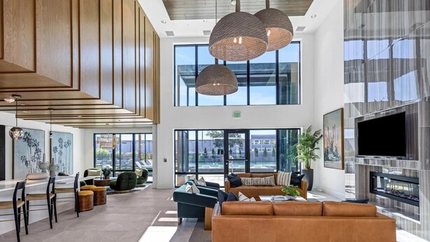 Eine großzügige Lobby mit hoher Decke, großen Fenstern, einer Sitzecke mit Sofas und einem an der Wand befestigten Flachbildfernseher.