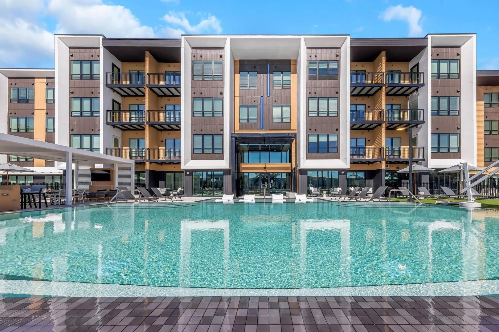 A modern building with a central pool, multiple balconies, and outdoor seating areas.