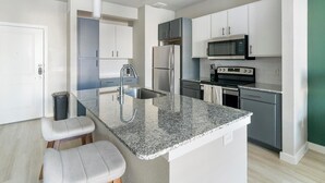 A modern kitchen with granite countertops, stainless steel appliances, and a central island with seating. - Landing | Chic 1BD, Game Room, Gym (Richmond)