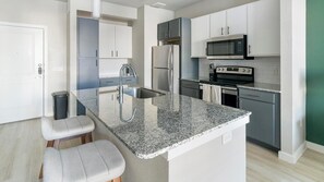 A modern kitchen with granite countertops, stainless steel appliances, and a central island with seating. - Landing | Chic 1BD, Game Room, Gym (Richmond)
