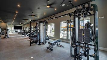 A gym with various exercise equipment, a bench, and a large window providing natural light.