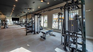 Un gimnasio con diversos equipos de ejercicio, una banca y un amplio ventanal que proporciona luz natural.