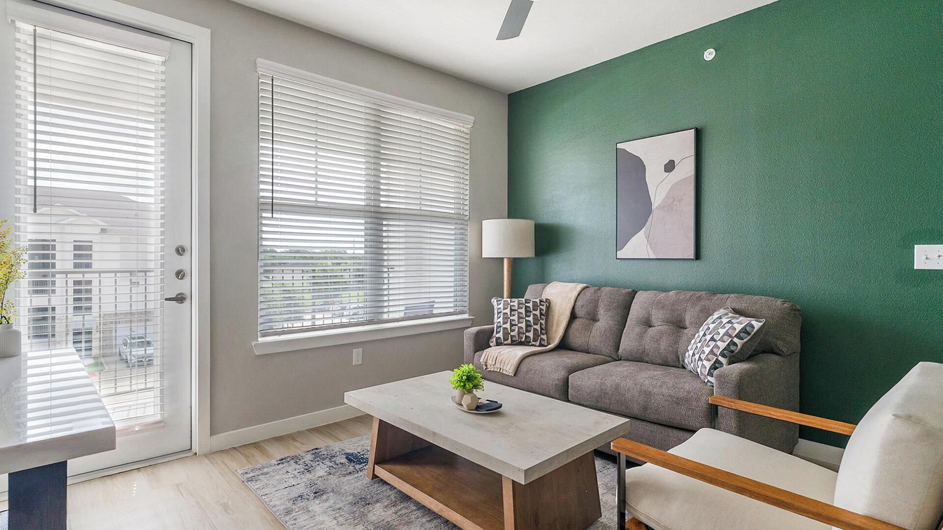 Un salon moderne avec un canapé gris, une table basse et un mur d’accent vert.