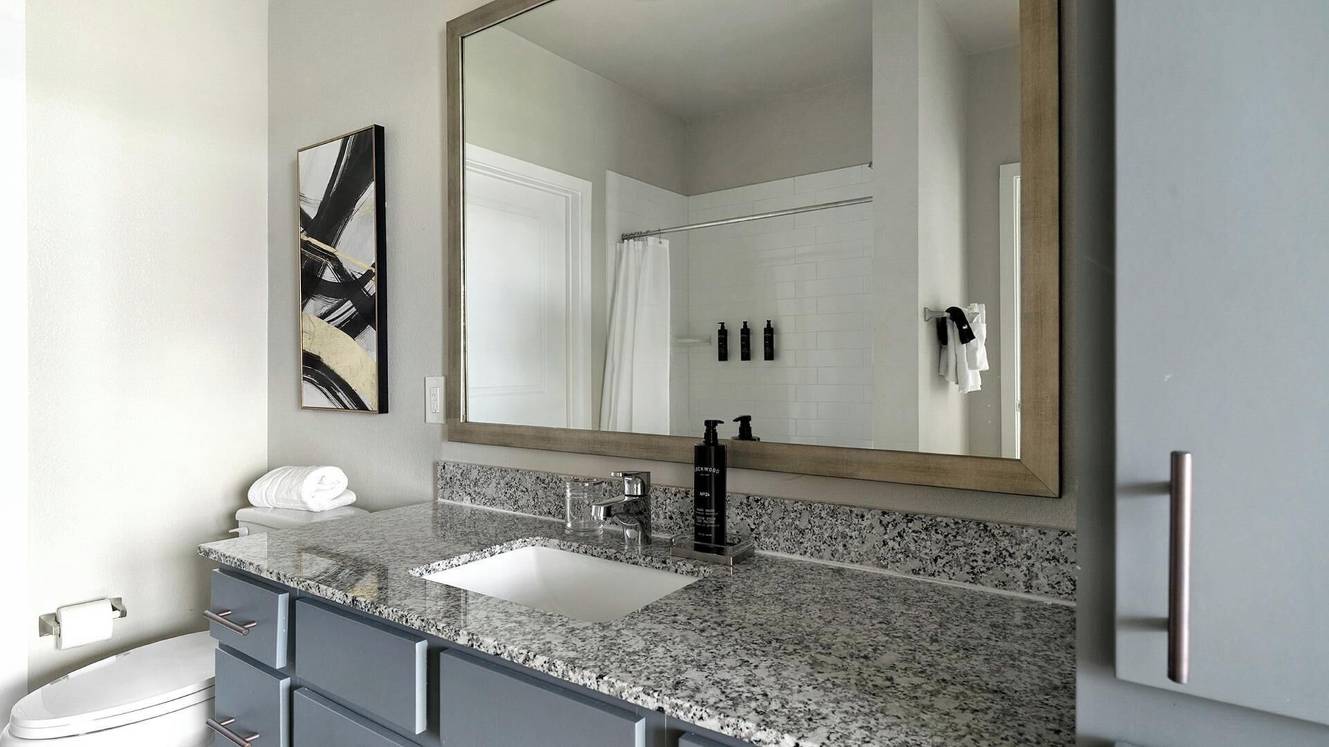 A bathroom with a large mirror, a sink, a toilet, and a towel rack.