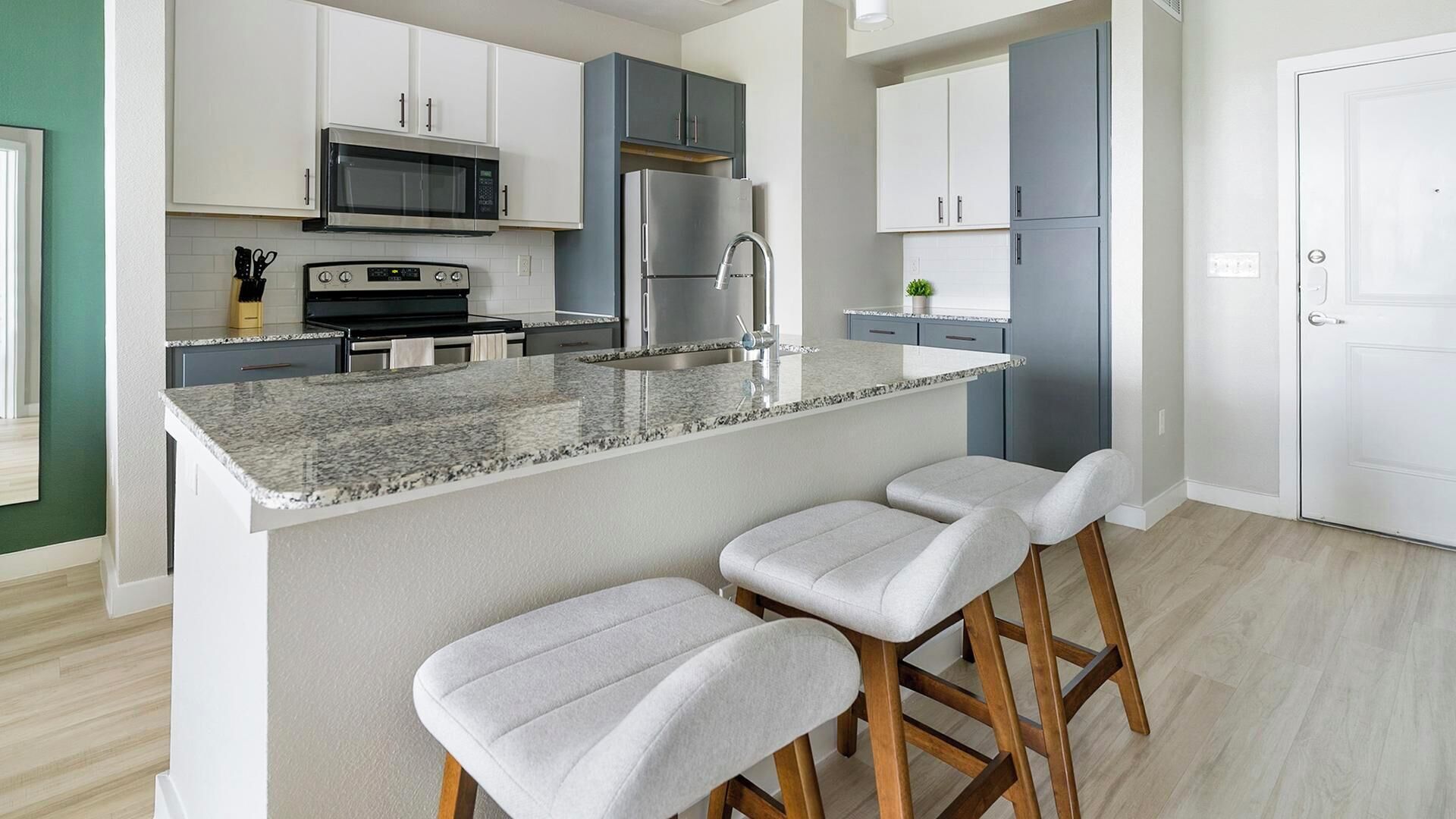 A modern kitchen with a central island, bar stools, a microwave, a stove, and a refrigerator.