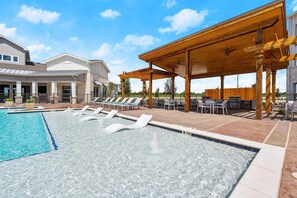 Une piscine avec des chaises longues, un patio couvert et un bâtiment à la façade en pierre.