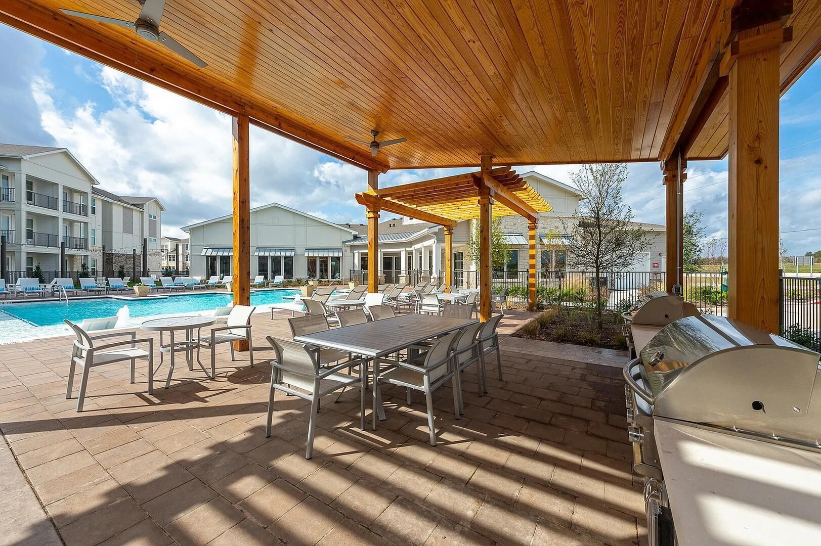 Une terrasse extérieure avec une piscine, des chaises longues, une table à manger et un barbecue.