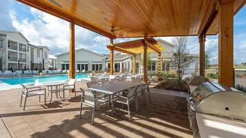 Une terrasse extérieure avec une piscine, des chaises longues, une table à manger et un barbecue.
