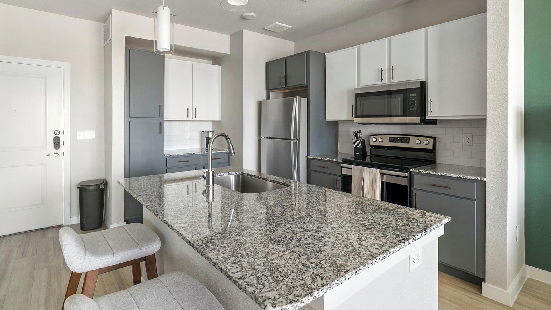 A modern kitchen with granite countertops, stainless steel appliances, and grey cabinetry.
