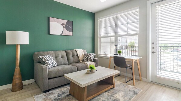 Un salon moderne avec un canapé gris, une table basse, une lampe et une fenêtre avec des stores.