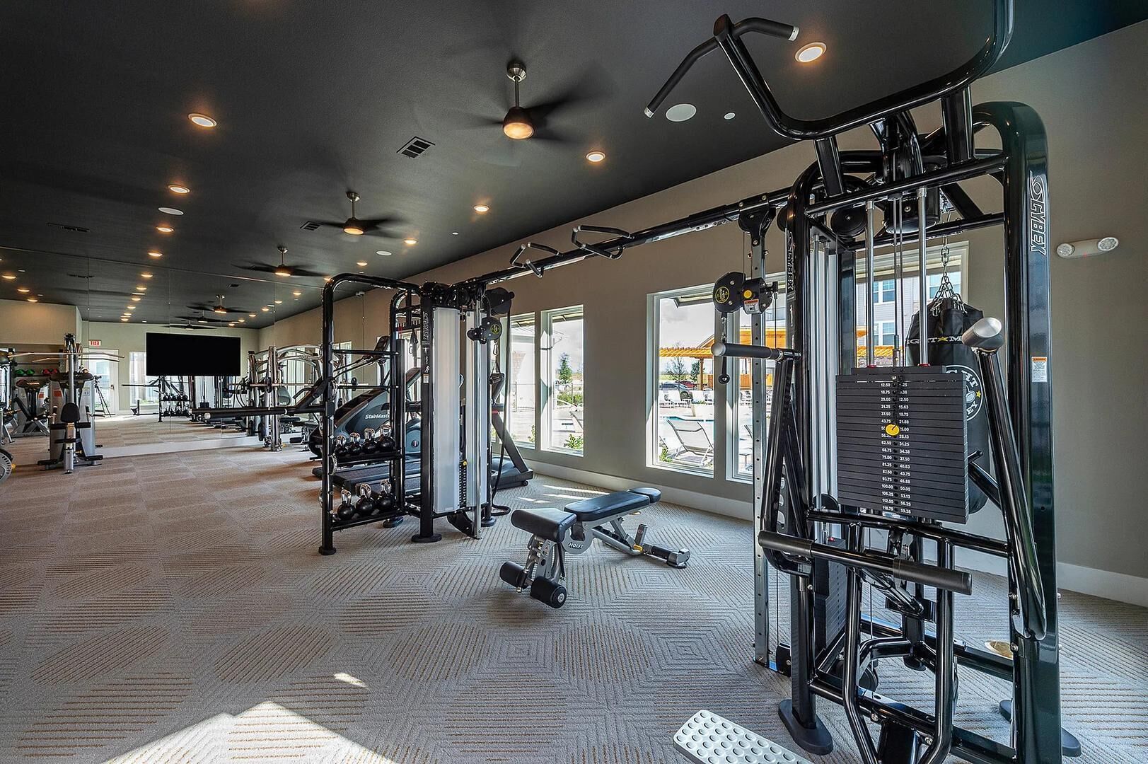 A gym with various exercise equipment, a bench, and a large window providing natural light.