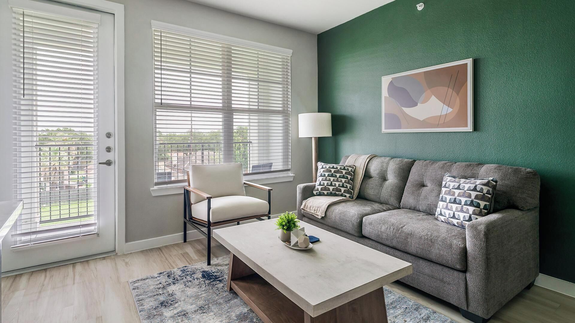 A living room with a grey sofa, a white armchair, a coffee table with a plant, and a green accent wall.