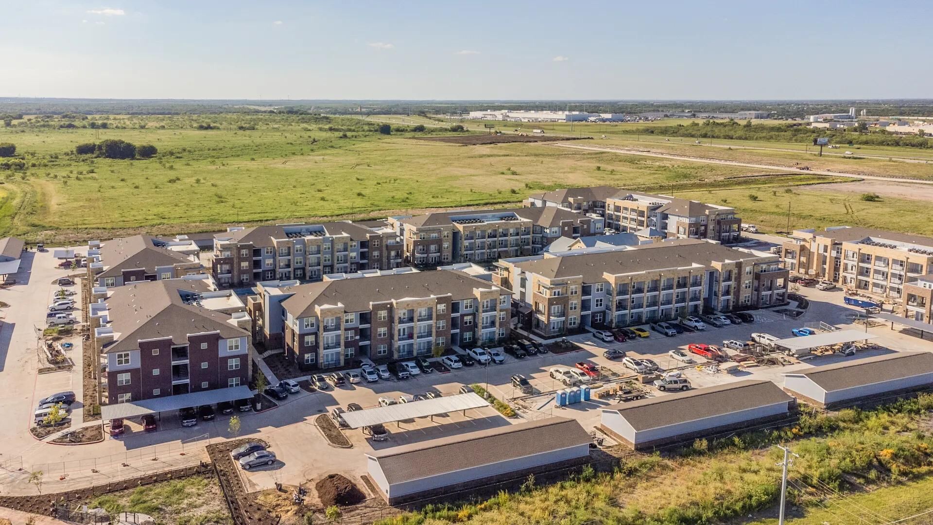 A multi-story apartment complex with a parking lot and a large open field in the background.