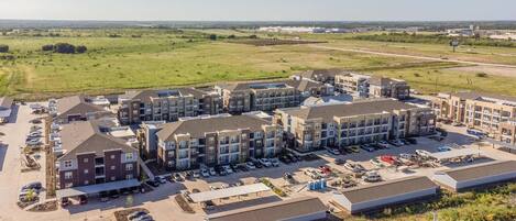 A multi-story apartment complex with a parking lot and a large open field in the background.
