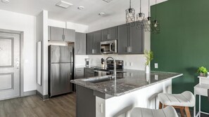A modern kitchen with stainless steel appliances, a granite countertop, and a green accent wall.