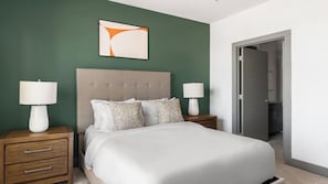 A bedroom with a large bed, two bedside tables with lamps, a headboard, and a door leading to a bathroom. - Landing | Chic 1BD, Gym (Terrell)
