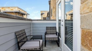 Eine kleine Terrasse im Freien mit zwei Korbstühlen und einem Tisch, einer Schiebetür aus Glas sowie Steinmauern.