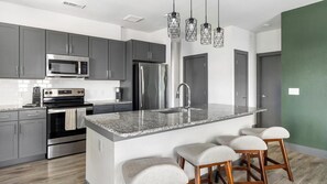 A modern kitchen with stainless steel appliances, grey cabinets, a granite countertop, and a bar stool seating area.