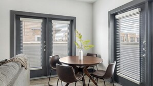 Et moderne spiseområde med et rundt bord, fire stole, en vase med blomster og store vinduer med persienner.