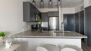 A modern kitchen with a central island, stainless steel appliances, and pendant lighting. - Landing | Beautiful 1BD, Gym (Terrell)