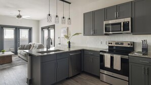 A modern kitchen with dark cabinets, a stainless steel microwave, an oven, and a dishwasher. - Landing | Beautiful 1BD, Gym (Terrell)