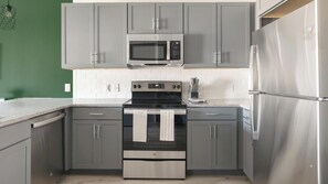 A kitchen with grey cabinets, a stainless steel refrigerator, a microwave, and an oven. - Landing | Stunning 1BD, Gym (Terrell)