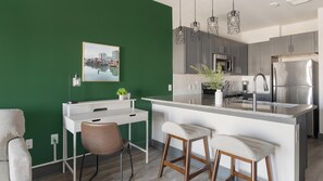 A modern kitchen with a green accent wall, a white island with bar stools, and a cityscape painting.