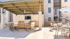 Eine Terrasse im Freien mit Grill, Sitzgelegenheit und einem an einer Steinwand befestigten Fernseher.