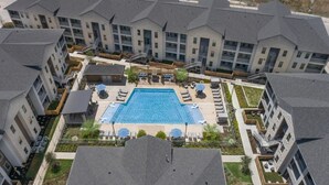 A modern apartment complex with a central swimming pool, outdoor seating, and a covered patio area. - Landing | Incredible 1BD, Gym, Clubhouse (Leander)