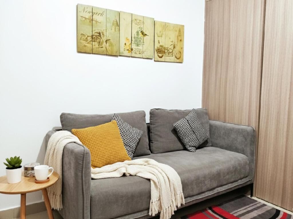 Un sofá gris con cojines estampados, una mesita con una planta y una taza, y una pared decorada con ilustraciones de estilo vintage.