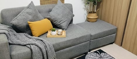 Un sofá gris con cojines, una planta pequeña y una bandeja con velas y otra planta.
