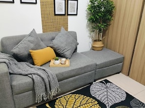 Un canapé gris avec des coussins, une petite plante et un plateau avec des bougies et une plante.