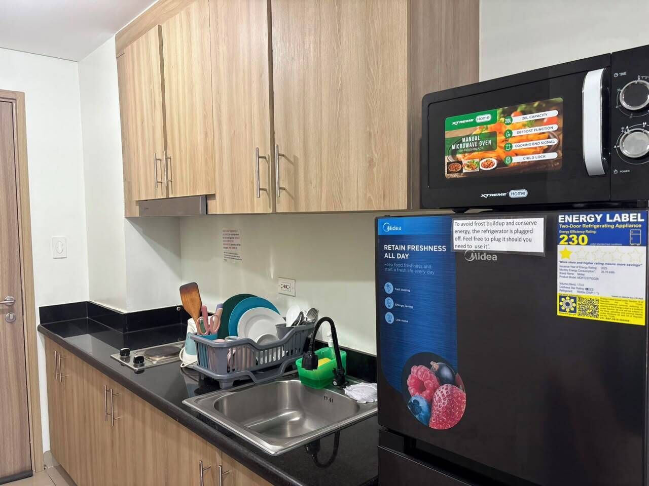 Una cocina con armarios de madera, un lavamanos de acero inoxidable y un refrigerador negro con etiqueta de eficiencia energética.