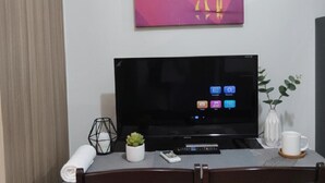 A hotel room with a flat-screen TV, a remote control, a smartphone, a rolled towel, a small potted plant, a white mug, and a decorative vase. - Mall of Asia - Asian Budget Stays (Pasay City)