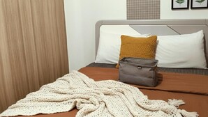 A bed with a brown bedspread, a white pillow, a mustard-colored pillow, a gray bag, and a white knitted blanket. - Mall of Asia - Asian Budget Stays (Pasay City)