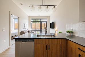 A modern kitchen with a dishwasher, wooden cabinets, a stainless steel sink, and a built-in oven. - Landing | Modern 1BD, Game Room, Gym (Salt Lake City)