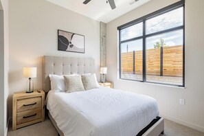 Un dormitorio con una cama grande, dos mesitas de noche, un ventanal y un ventilador de techo.