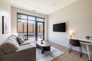 Un salon moderne comprenant un canapé, une table basse, un bureau et un téléviseur fixé au mur.