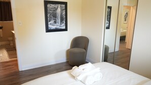 Une chambre d’hôtel avec un lit, une chaise, un miroir et un tableau encadré au mur.