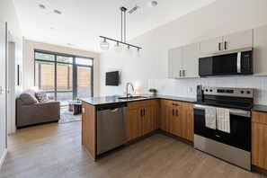 A modern kitchen with a dishwasher, microwave, stove, and wooden cabinets. - Landing | Incredible 1BD, Courtyard, Gym (Salt Lake City)