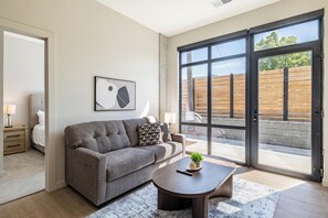 A modern living room with a grey sofa, a coffee table, and a large sliding glass door leading to an outdoor area. - Landing | Incredible 1BD, Courtyard, Gym (Salt Lake City)