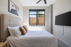Une chambre à coucher avec un lit, une fenêtre, un téléviseur et une œuvre d’art accrochée au mur.
