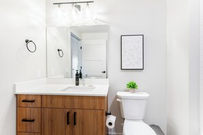 Une salle de bain moderne avec un lavabo blanc, un meuble-lavabo en bois, un miroir, des toilettes et un tableau encadré au mur.
